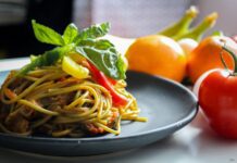 pasta with vegetable dish on gray plate beside tomato fruit on white table